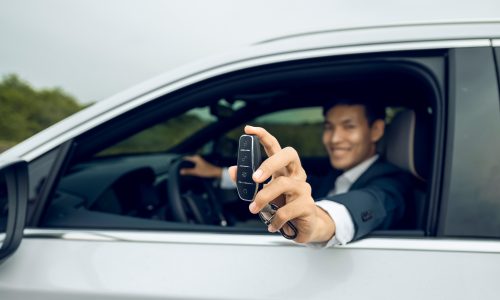 Businessman holding modern car keys, alarm system and steering wheel with electric buttons - male hand holding keys