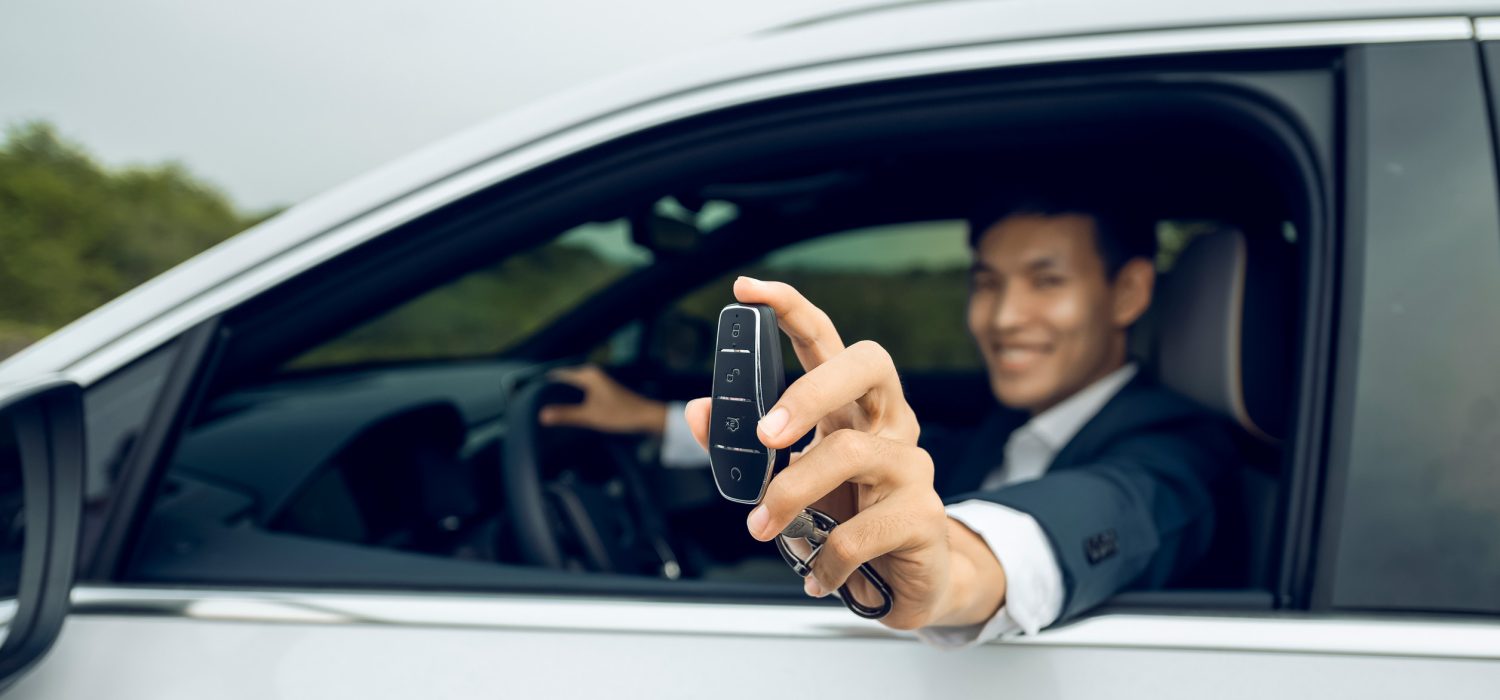 Businessman holding modern car keys, alarm system and steering wheel with electric buttons - male hand holding keys